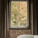 Soft daylight through a bedroom window framing autumn trees with orange and green leaves