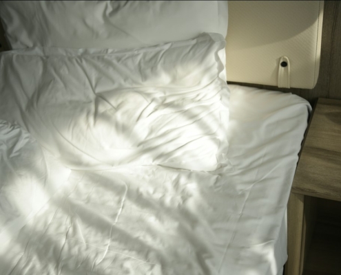 Soft morning sunlight falling across a white bed with rumpled sheets and pillows