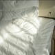 Soft morning sunlight falling across a white bed with rumpled sheets and pillows