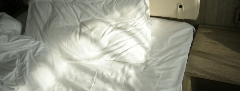 Soft morning sunlight falling across a white bed with rumpled sheets and pillows
