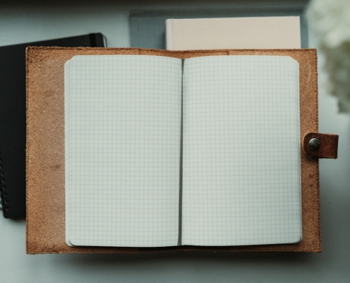 Open blank grid-paper journal in a leather cover on a desk beside white flowers, for keeping a daily medication and mood log