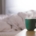 A green ceramic mug on a bedside table beside an unmade bed in soft morning light
