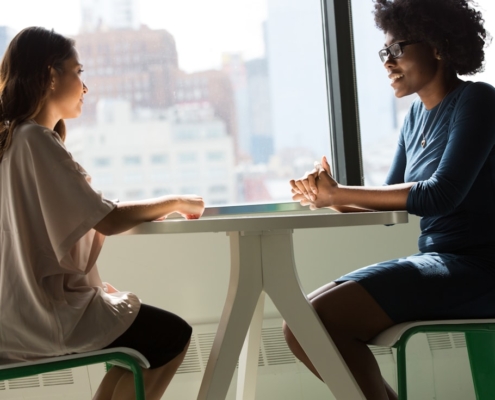 Two people in a warm supportive conversation across a table by a window