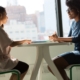 Two people in a warm supportive conversation across a table by a window