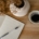 An open lined journal with a pen beside a cup of coffee and dried flowers on a wooden table