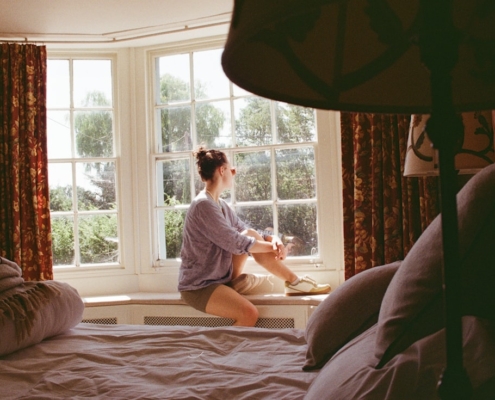 Person sitting quietly in a sunlit bay window, reflecting on whether to seek residential care