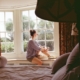 Person sitting quietly in a sunlit bay window, reflecting on whether to seek residential care